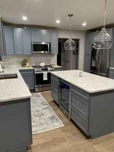 a large kitchen with gray cabinets and marble counter tops, stainless steel appliances and an island in the middle