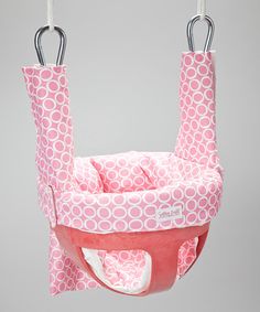 a pink and white baby seat hanging from a hook on a gray background with circles