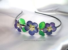 a purple flower headband with green leaves and beads on the side is laying on a white sheet