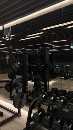 an empty gym with rows of dumbs and weight machines in the foreground, all lit up by recessed lights