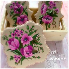 four decorated cookies in a box with pink flowers on the front and purple flowers on the back