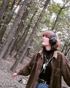 a woman walking in the woods with headphones on her ears and looking up at something