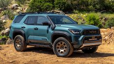 a blue truck parked on top of a dirt road next to rocks and trees in the background