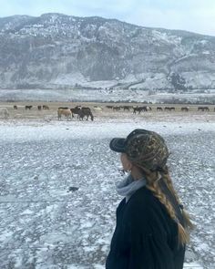 a woman standing in the snow looking at horses