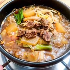 a bowl of beef and vegetable soup with chopsticks next to it on a table