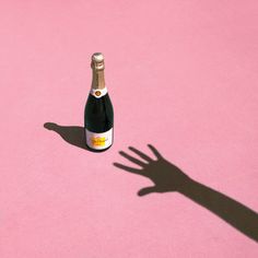 the shadow of a hand on a pink surface with a bottle of wine in it