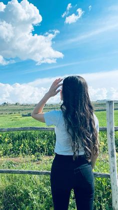 a woman standing in front of a fence looking at the sky with her hands on her head