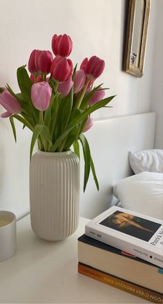 a white vase filled with pink tulips on top of a table next to a stack of books