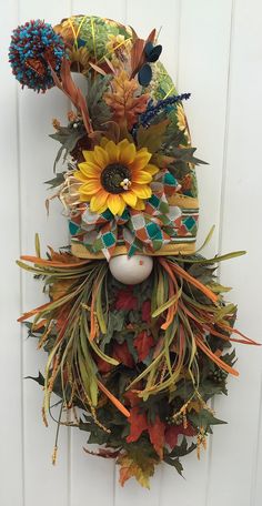 a wreath with sunflowers and feathers hanging on a white door, in front of a wall