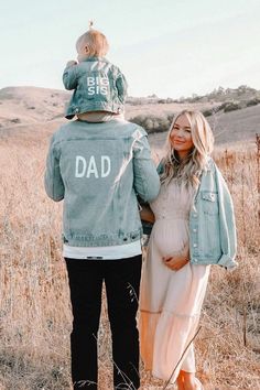 a man and woman standing in a field with their child on their shoulders, both looking at each other