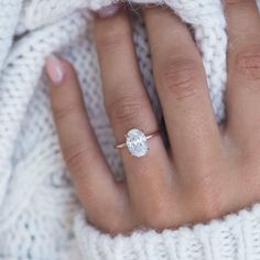 a woman's hand with a diamond ring on her finger, wearing a white sweater