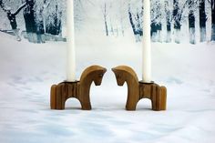 two candles are placed next to each other in the snow, with one horse shaped candle holder between them