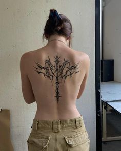 a woman with a tattoo on her back is standing in front of a white wall