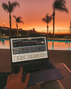 a person sitting in front of a laptop computer on top of a table next to a swimming pool