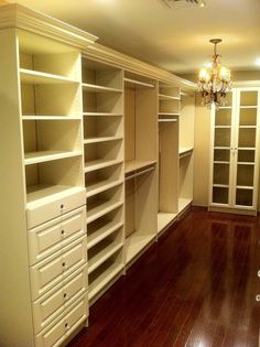 an empty room with lots of white shelves and drawers on the wall, in front of a chandelier