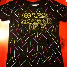 a t - shirt that says, 100 days smarter he is on top of a wooden table