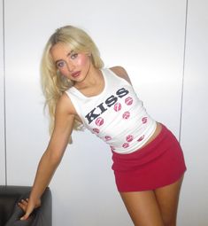 a woman posing in a white shirt and red skirt with her hand on the wall