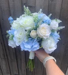 a bouquet of white and blue flowers is held by a woman's hand in front of a wooden fence