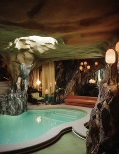 an indoor swimming pool surrounded by large rocks and trees with lamps on the ceiling above it