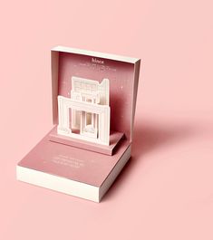 an open box with a model of a building inside it on a pink background,