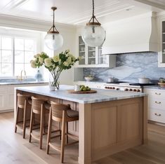 a kitchen with marble counter tops and wooden stools in front of an island topped with flowers