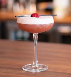 a drink with a raspberry garnish on the rim sits on a table