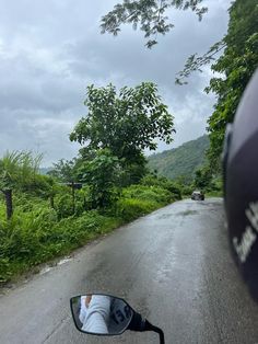 a person is taking a photo from the side mirror of a motorcycle on a country road