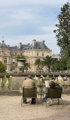 two people sitting on chairs in front of a large building with trees and flowers around them