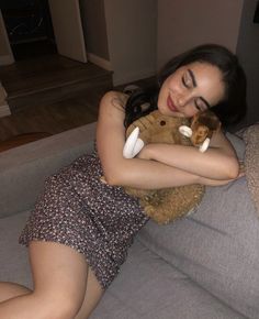 a woman laying on top of a couch holding a stuffed animal in her arms and smiling at the camera