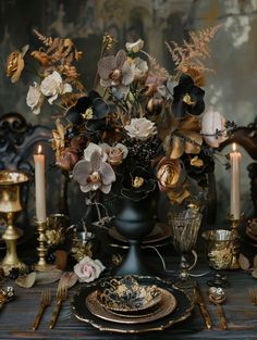 the table is set with black and gold plates, silverware, and floral centerpieces