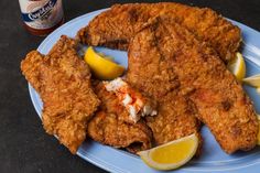 fried chicken with lemon wedges on a blue plate next to a can of beer