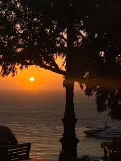 the sun is setting over the water and boats are in the ocean behind some trees