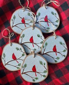 four ornaments with red birds on them are sitting on a plaid tablecloth and one is hanging from a string