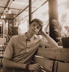 a young man sitting on top of a wooden bench next to a potted plant