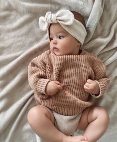 a baby is laying on a bed wearing a sweater and a headband