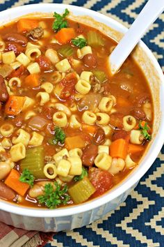 a white bowl filled with pasta and vegetable soup on top of a checkered table cloth