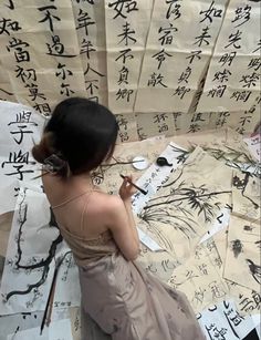 a woman in a dress is writing on paper with chinese characters behind her and another person holding a pen