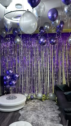 balloons and streamers are hanging from the ceiling in front of a purple backdrop with silver balls