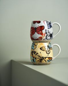 three coffee cups are stacked on top of each other, with butterflies painted on them