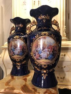 two blue vases sitting on top of a marble table next to a mirror with gold trimming