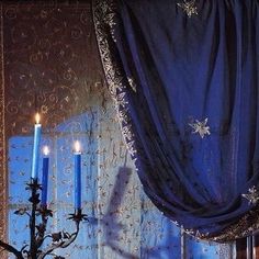 two candles are lit in front of a window with blue drapes and curtains behind it