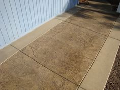 a cement sidewalk next to a building with blue siding on the wall and dirt around it