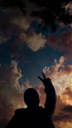 the silhouette of a person and a cat in front of a cloudy sky at sunset