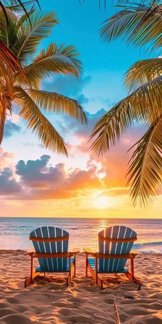 two blue chairs sitting on top of a sandy beach next to the ocean at sunset