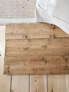 a bed with white sheets and wood flooring next to a wooden planked wall