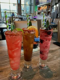 three different colored drinks sitting on top of a wooden table