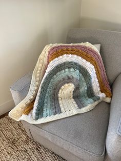 a crocheted rainbow afghan sits on a grey couch with a gray arm chair