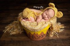 a newborn baby is sleeping in a yellow basket on a wooden floor wearing a knitted hat