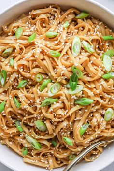 a white bowl filled with sesame seed noodles and topped with scallions on top