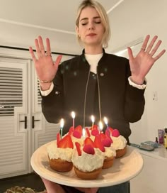 a woman holding a plate with cupcakes and strawberries on it in front of her